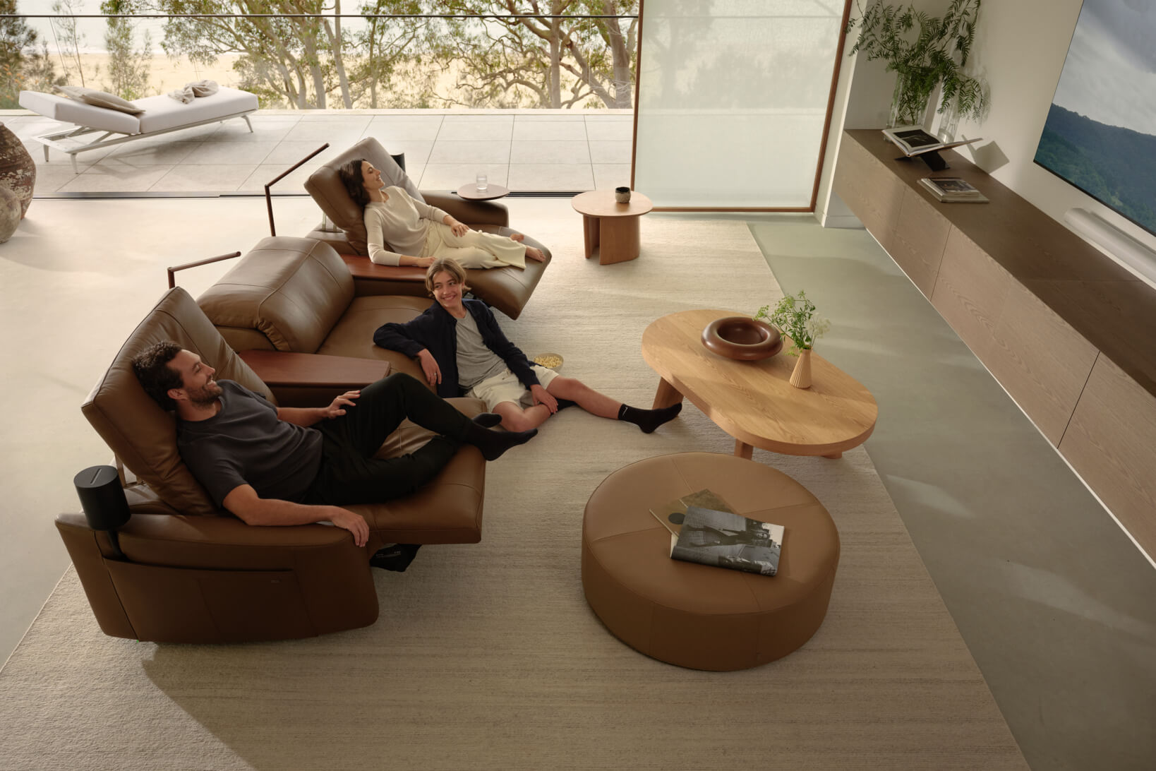 A family relax on a brown leather recliner sofa in a modern living room with timber accents.